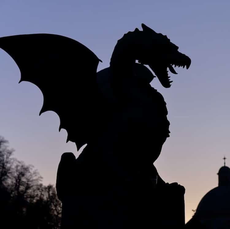The fire Dragon symbol of the city of Ljubljana, seen on city bridge. Night silhouette against purple sky, with skyline